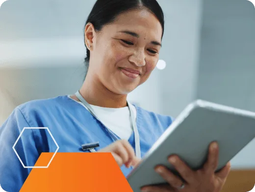 Smiling healthcare professional in scrubs using a digital tablet, with abstract orange and hexagon graphic elements in the foreground.